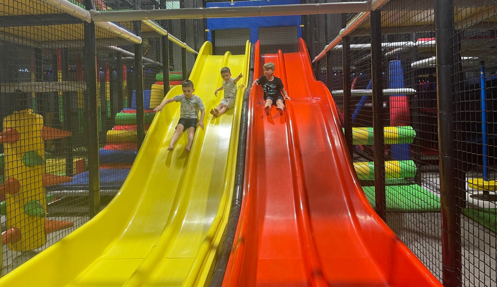 Children racing down the yellow and orange wave slides indoors